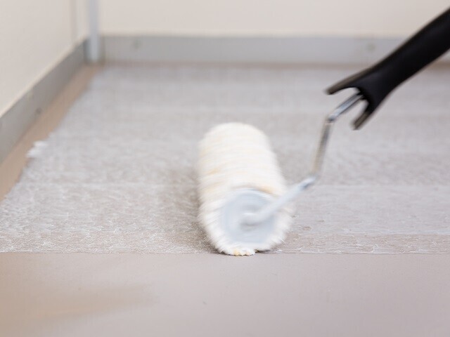 Adhesive being applied with a roller to the subfloor