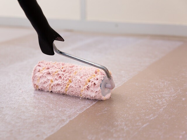 Pink roller applying adhesive to the subfloor