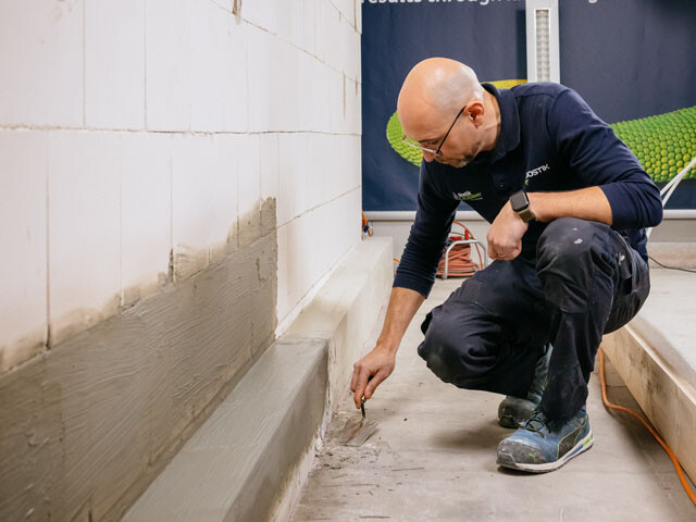 Guy kneeling to apply grout to waterproof concrete