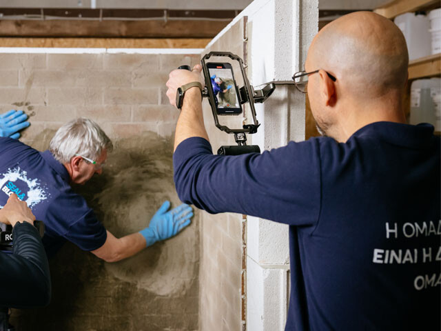 Two guys recording a thrid who's applying grout to waterproof