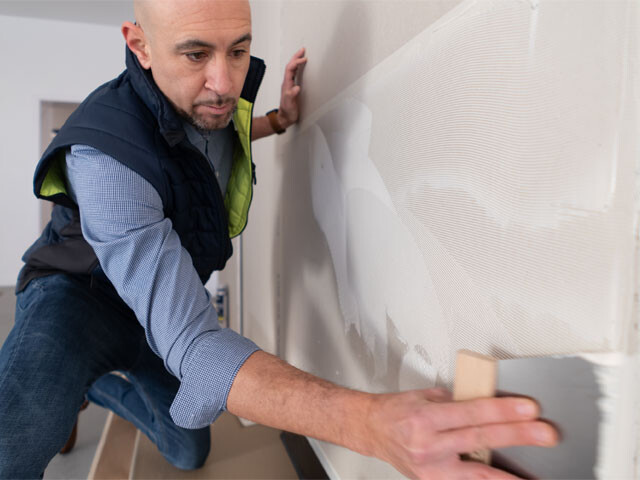 Guy applying adhesive to a wall with a trovel